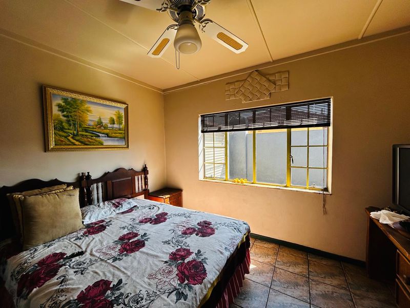 A functional bedroom featuring tiled flooring, a ceiling fan, and a window with security bars, offering a standard layout for a residential home.