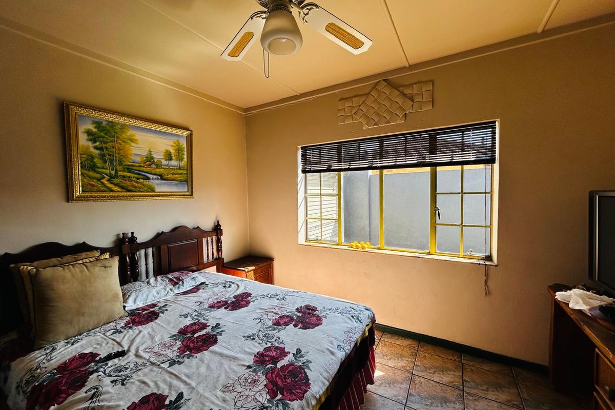 A functional bedroom featuring tiled flooring, a ceiling fan, and a window with security bars, offering a standard layout for a residential home.
