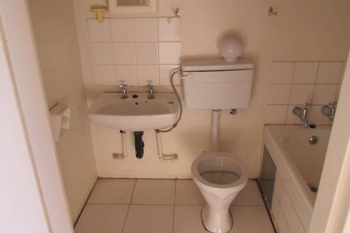 A compact, dated bathroom featuring a wall-mounted basin, standard toilet, and bathtub with tiled splashbacks and flooring, requiring modernization.