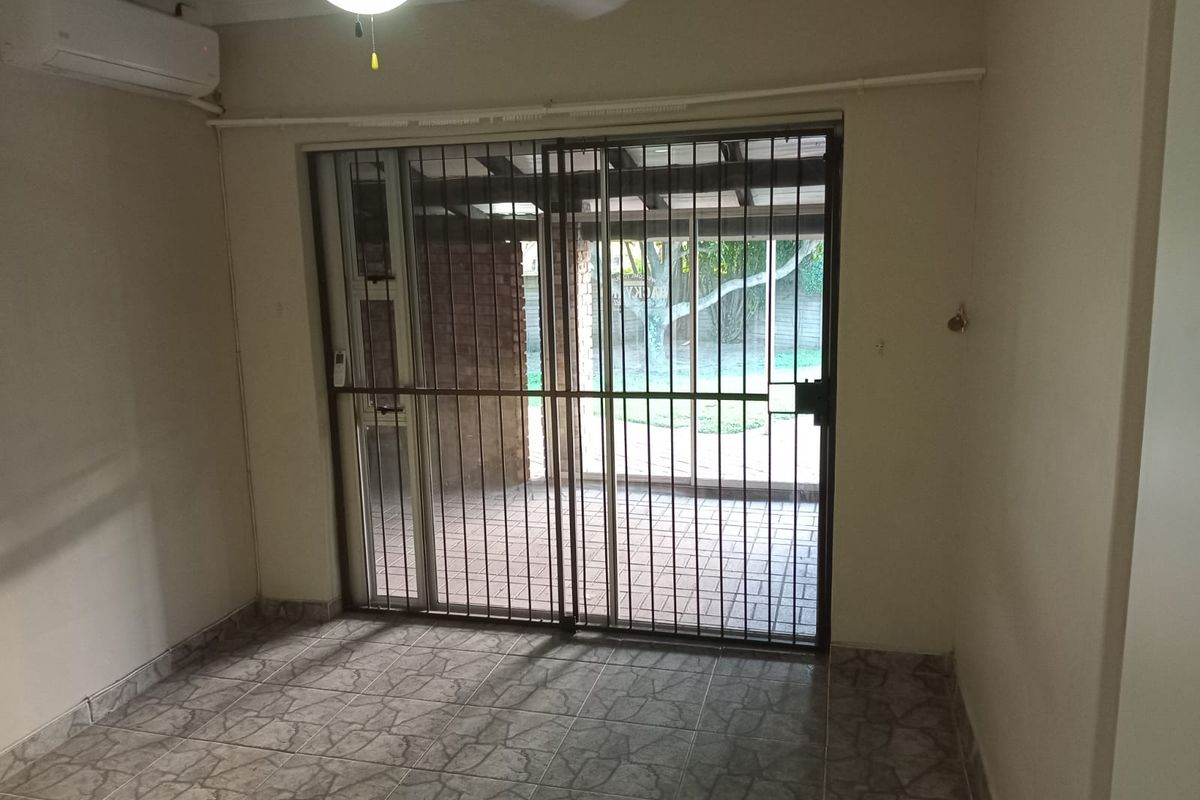 An empty living room featuring tiled flooring, a ceiling fan, a wall-mounted air conditioner, and a sliding glass door with a security gate leading outside.