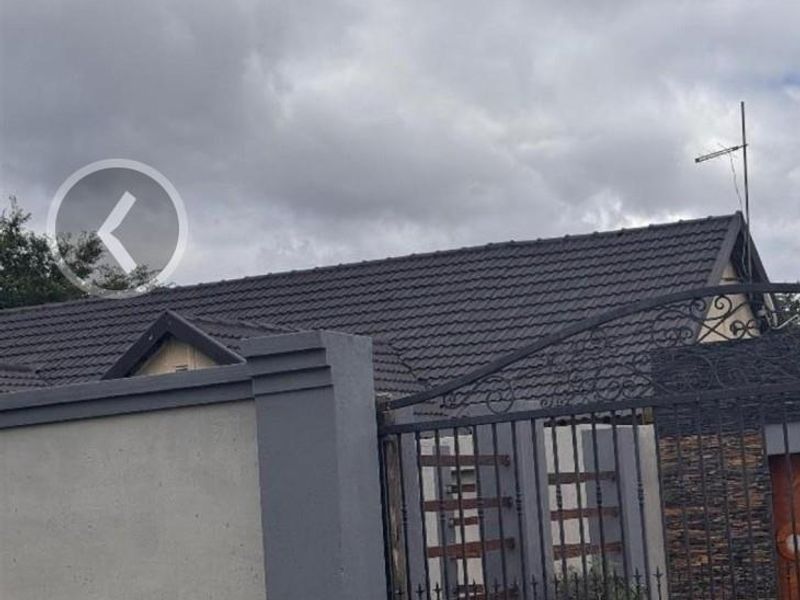 Front exterior view of the property featuring a tiled roof, secure wrought iron gate, and stone cladding on the boundary wall.