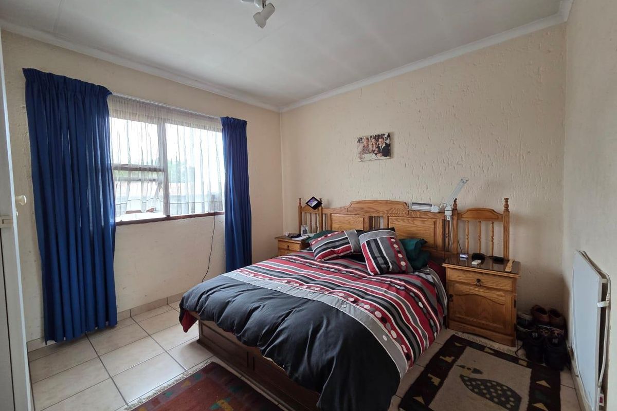 A standard bedroom featuring tiled flooring, textured walls, and a window with curtain tracks.