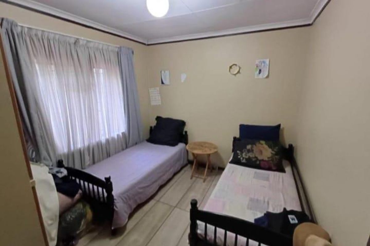A functional bedroom featuring tiled flooring and a large window with curtains, providing a simple and practical living space.