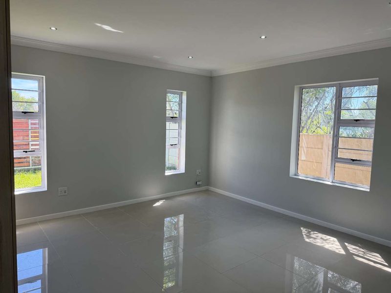 A bright, empty living room featuring polished tiled flooring, recessed downlights, and large aluminium-framed windows providing ample natural light.