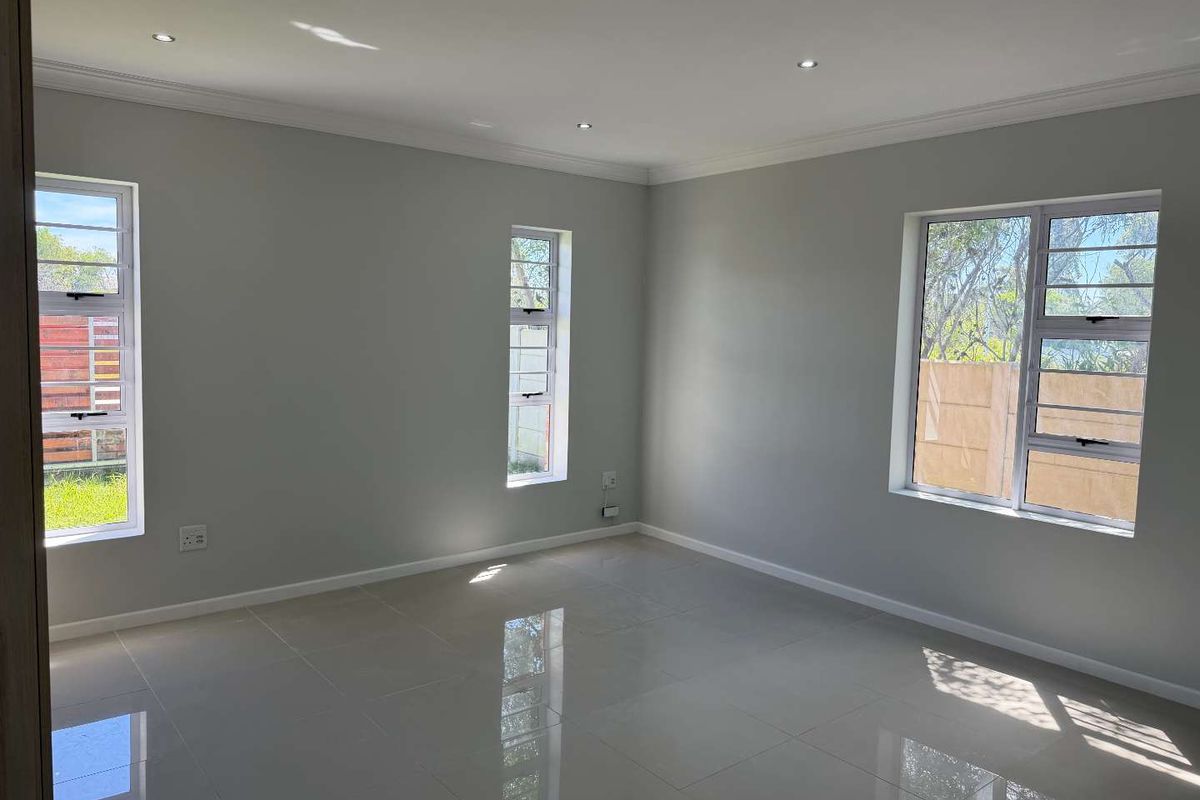 A bright, empty living room featuring polished tiled flooring, recessed downlights, and large aluminium-framed windows providing ample natural light.