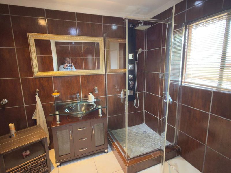 A bathroom featuring dark brown wall tiles, a glass vessel sink vanity, and a glass-enclosed shower with a modern shower panel.