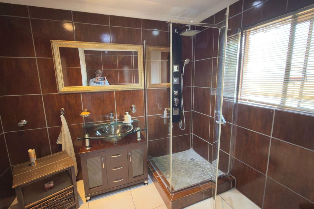 A bathroom featuring dark brown wall tiles, a glass vessel sink vanity, and a glass-enclosed shower with a modern shower panel.