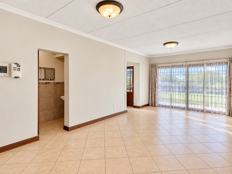 Spacious, light-filled living area featuring neutral tiled flooring, large sliding doors with security gates, and direct access to the garden.