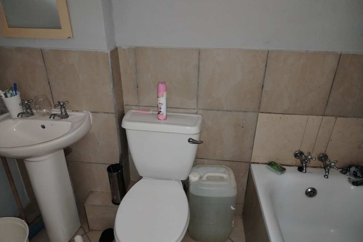 A functional bathroom featuring a pedestal basin, standard toilet, and a bathtub with wall-mounted taps and tiled splashbacks.