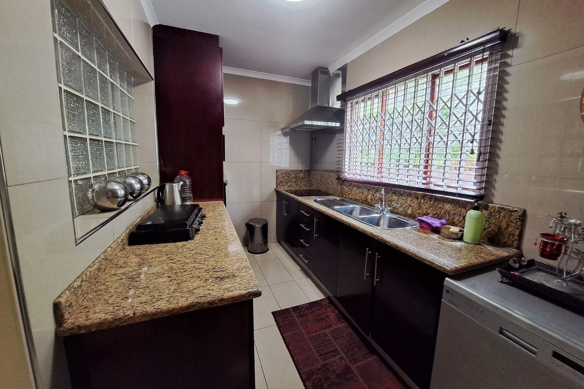 A functional kitchen featuring granite countertops, dark cabinetry, a stainless steel double sink, and a unique glass block feature wall.