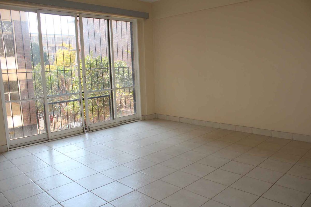 A bright, empty living area featuring neutral tiled flooring and a large sliding glass door with security bars, providing access to the exterior.