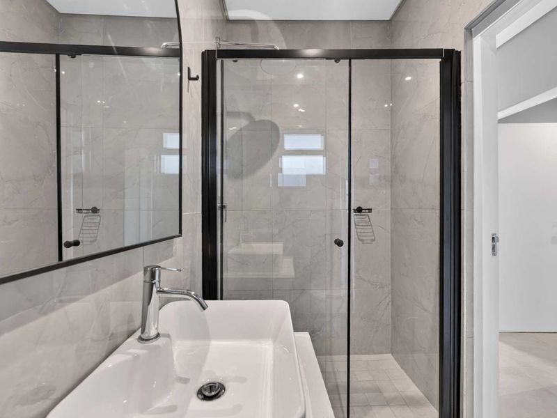 Modern bathroom featuring a walk-in shower with a black-framed glass screen, a sleek basin with chrome faucet, and contemporary grey wall tiling.