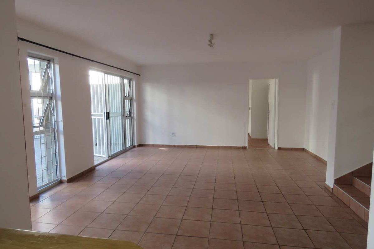 Spacious, empty living area featuring neutral tiled flooring, large sliding glass doors with security gates, and access to an adjoining room and staircase.