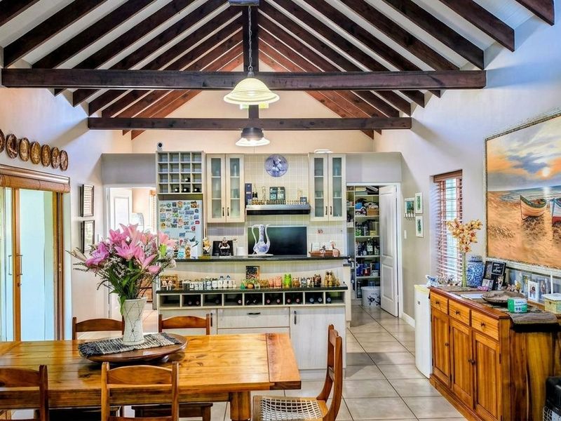 Spacious open-plan living and dining area featuring a striking vaulted ceiling with exposed timber rafters, tiled flooring, and a well-appointed kitchen with pantry.