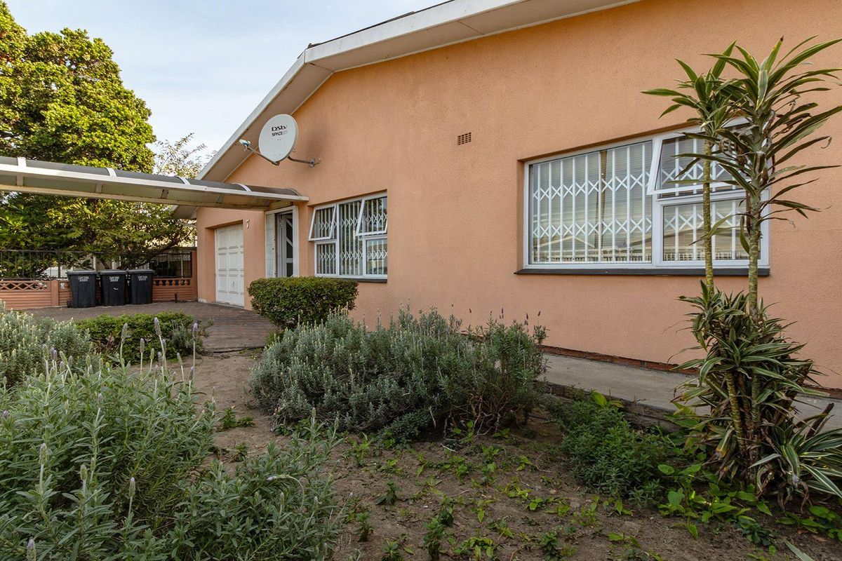 Rear exterior view of the house featuring a paved driveway, covered walkway, and security bars on the windows.