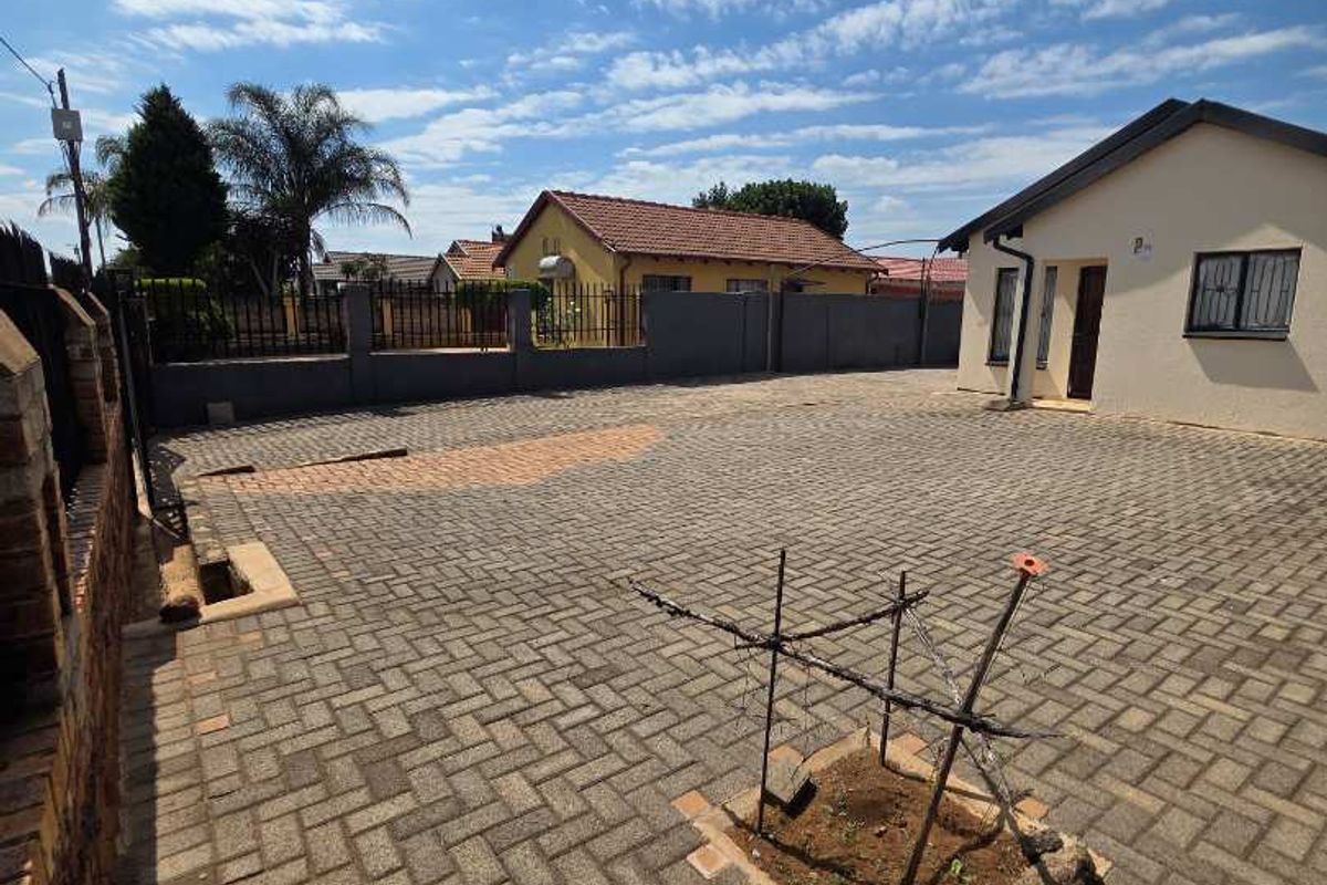 A paved exterior courtyard area featuring perimeter walling, security fencing, and a small central garden bed.