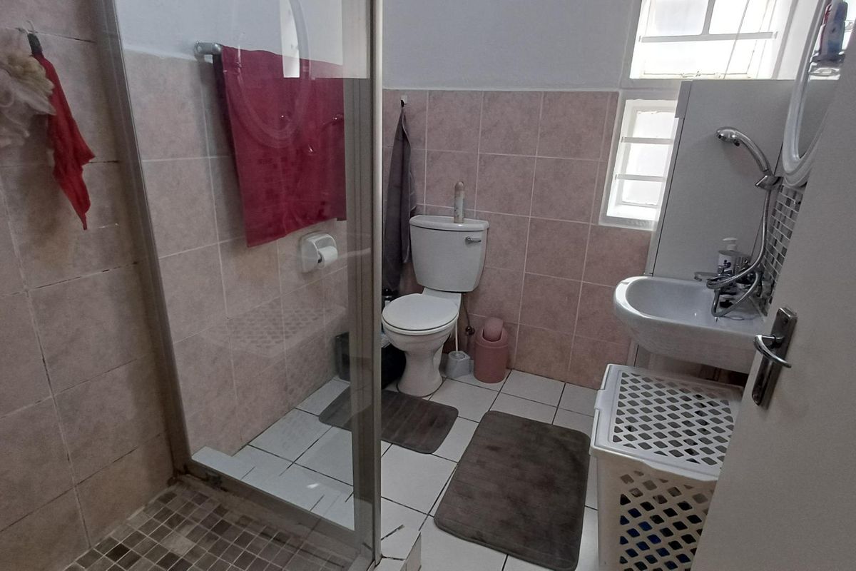 A functional bathroom featuring a glass-enclosed shower, a standard toilet, and a wall-mounted basin with tiled finishes.