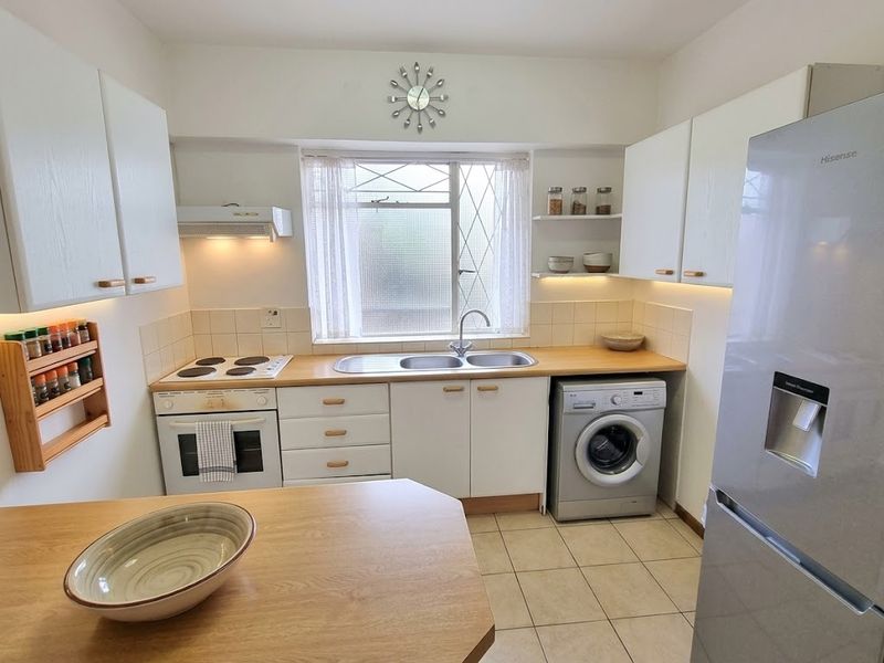 A functional kitchen featuring white cabinetry, wooden countertops, a built-in electric oven and hob, and integrated laundry plumbing.