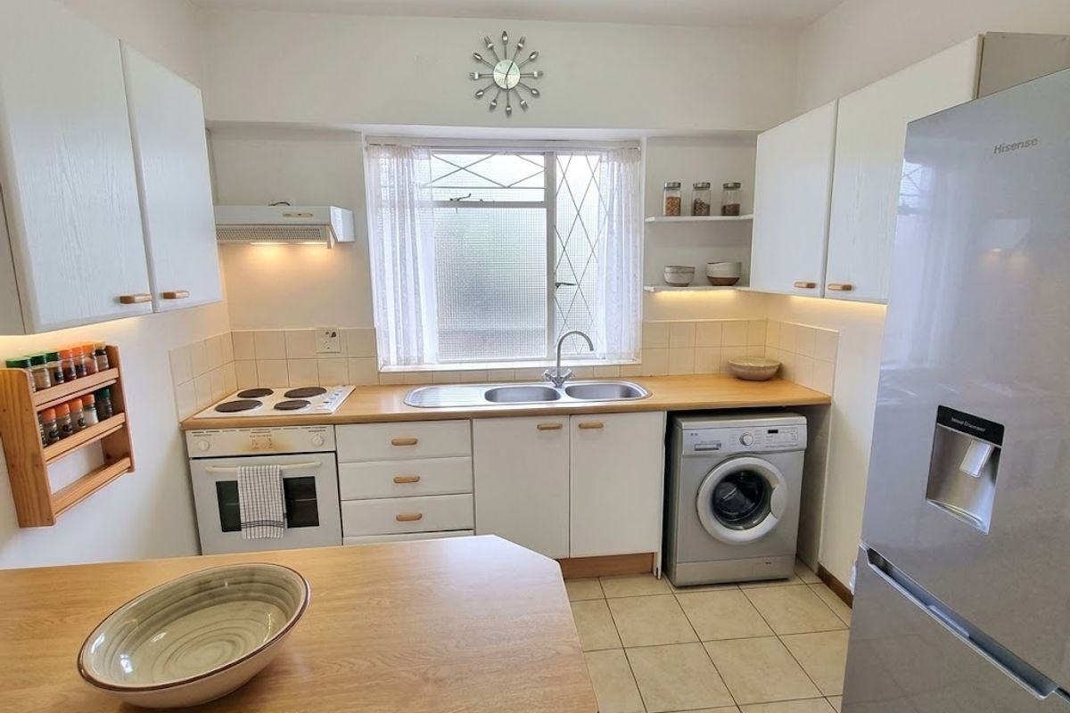A functional kitchen featuring white cabinetry, wooden countertops, a built-in electric oven and hob, and integrated laundry plumbing.