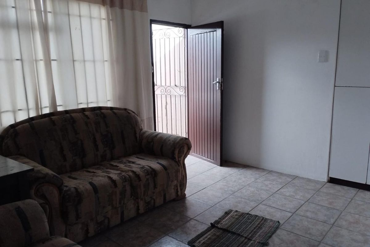A living room area featuring tiled flooring, a security gate at the entrance, and a built-in cupboard.