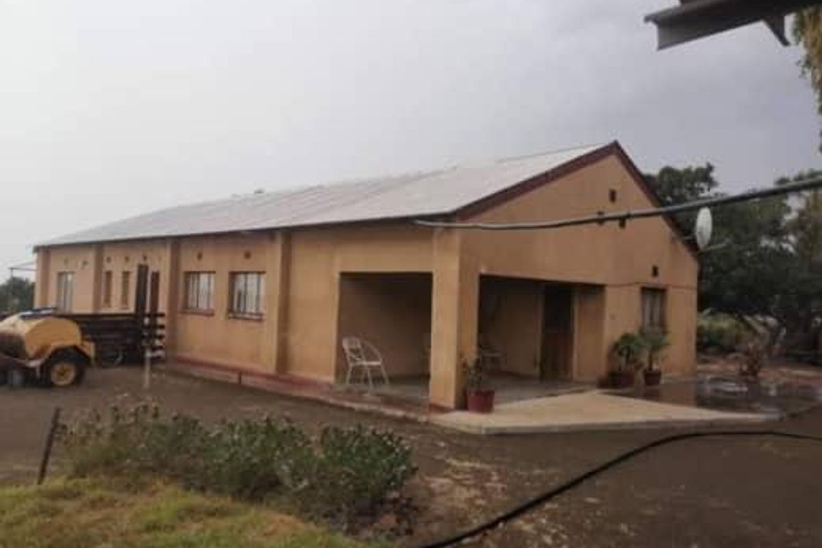 Exterior view of a single-story farm dwelling featuring a covered patio area, metal roof, and surrounding open land.