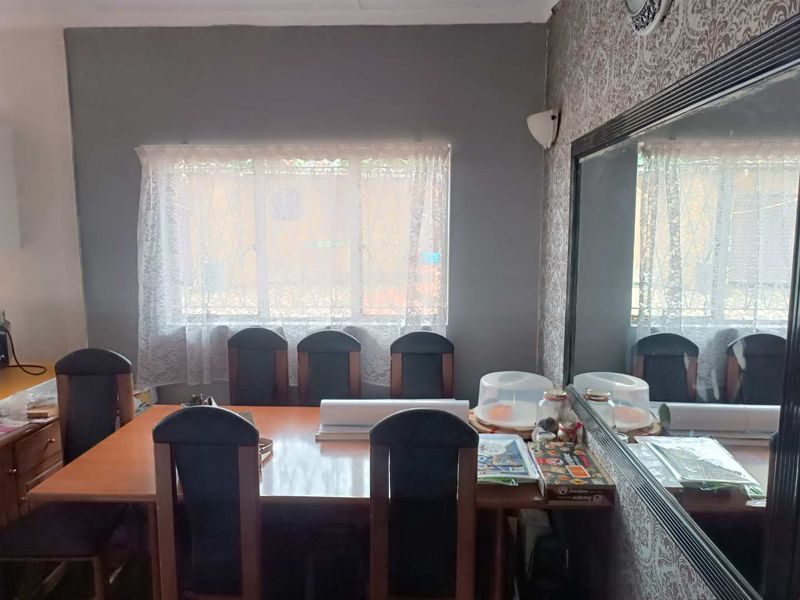 A dining room featuring a large wall-mounted mirror, a window with natural light, and decorative wallpaper.