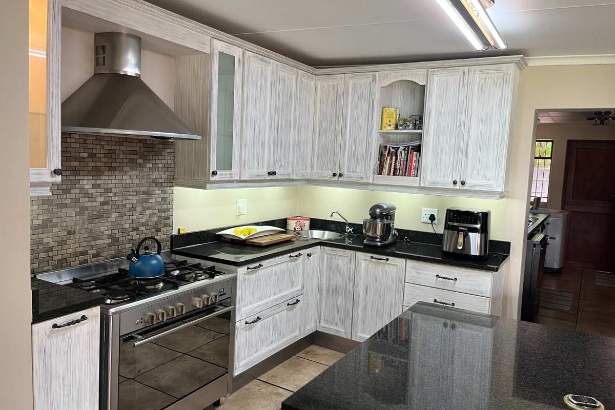 A well-maintained kitchen featuring white-washed cabinetry, granite countertops, a mosaic tile backsplash, and a stainless steel gas stove with an extractor fan.