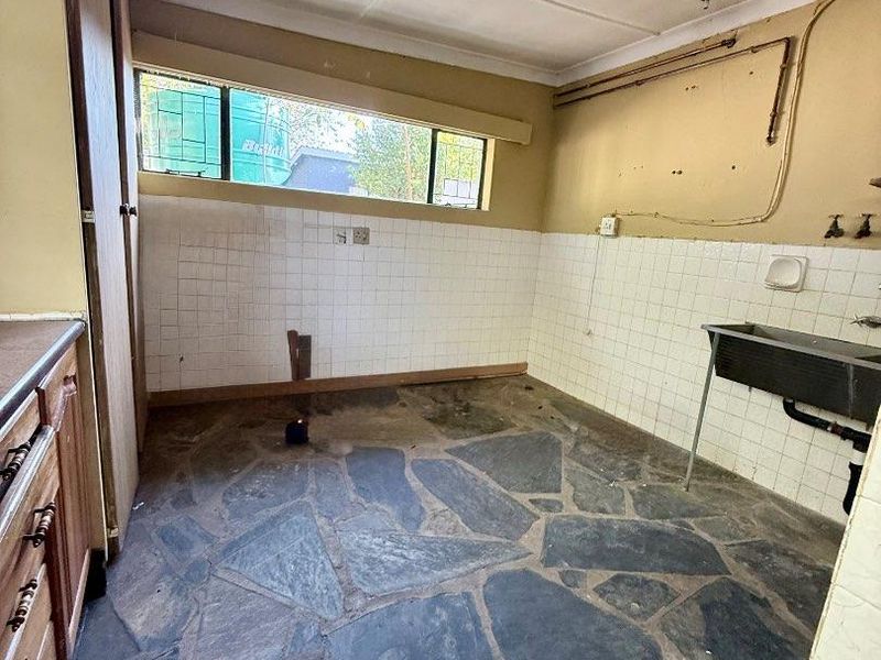A functional laundry room featuring a stainless steel utility sink, slate flooring, and built-in cabinetry, offering a blank canvas for renovation.