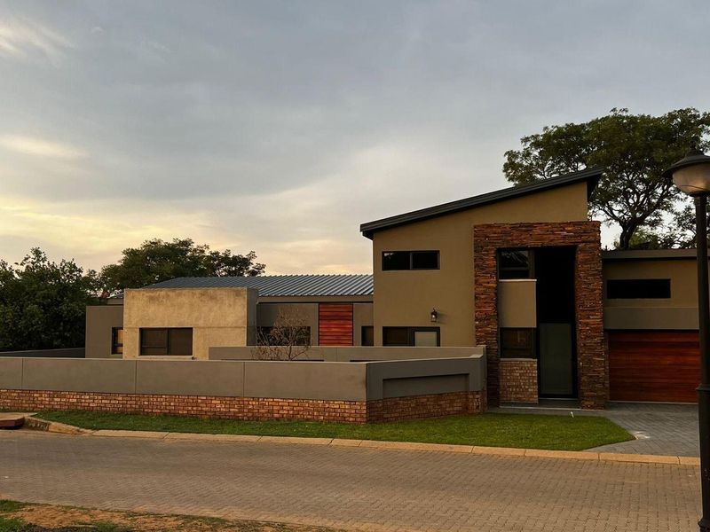 Modern architectural home featuring a striking stone-clad entrance, skillion roof design, and a paved driveway with a secure boundary wall.