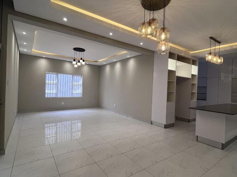Spacious open-plan living and kitchen area featuring modern recessed ceiling lighting, cove lighting, and high-gloss porcelain floor tiles throughout.
