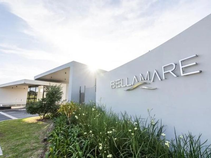The modern entrance facade of Bellamare apartment complex, featuring clean architectural lines, professional signage, and well-maintained landscaped gardens.