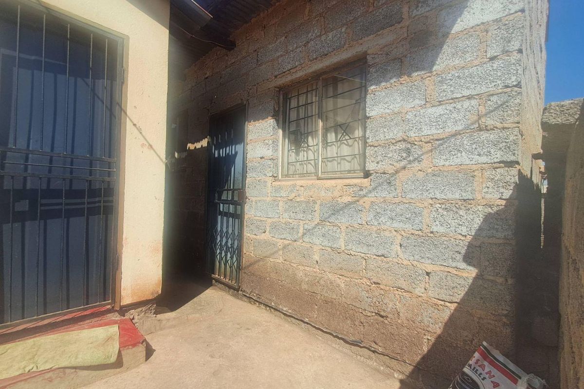Rear exterior view of the property featuring concrete block walls, security gates, and a concrete patio area.