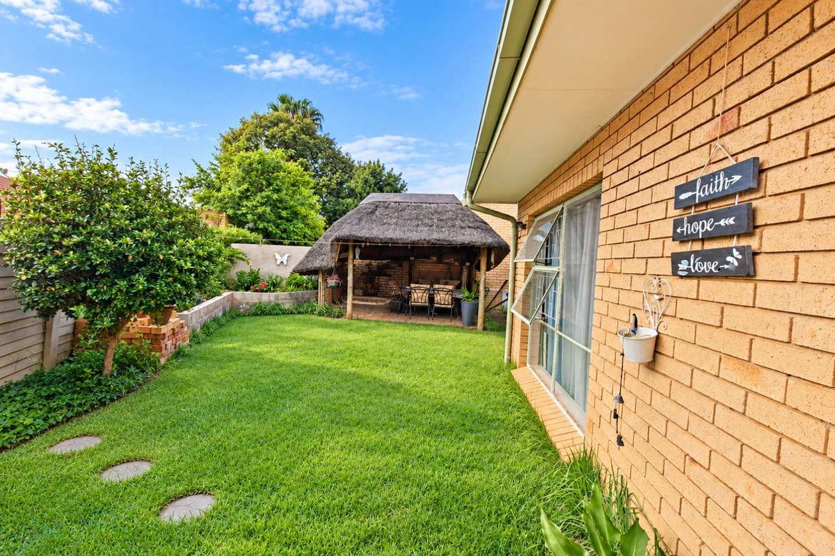 A well-maintained rear garden featuring a brick exterior, a lawn area, and a traditional thatched lapa for outdoor entertainment.