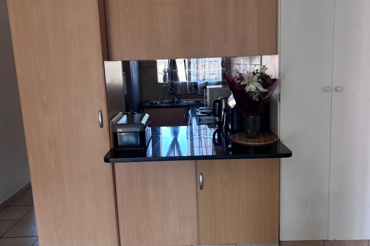 A compact kitchen featuring light wood-finish cabinetry, a dark granite countertop, and a mirrored splashback, providing a functional and efficient workspace.