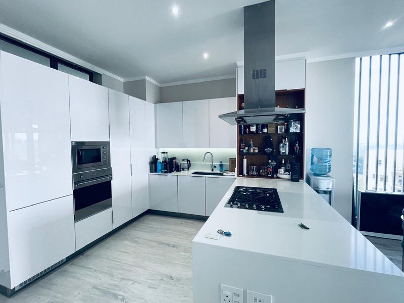 Modern kitchen featuring high-gloss white cabinetry, integrated appliances, a central island with a gas hob, and sleek quartz countertops.