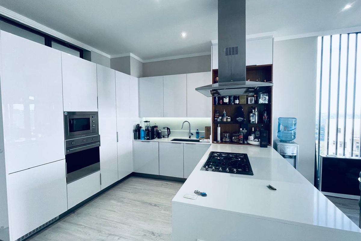Modern kitchen featuring high-gloss white cabinetry, integrated appliances, a central island with a gas hob, and sleek quartz countertops.
