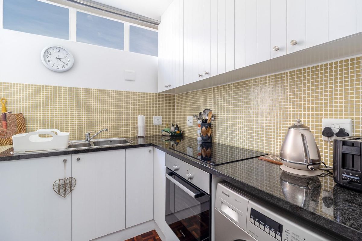 A compact, functional kitchen featuring white cabinetry, granite countertops, a mosaic tile backsplash, and integrated appliances including an oven, cooktop, and dishwasher.