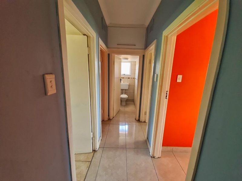 A functional hallway featuring tiled flooring, built-in overhead storage, and access to multiple rooms, including a bathroom at the end of the passage.