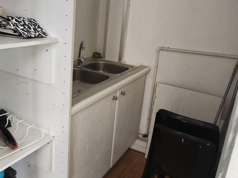 A compact scullery or utility area featuring a double stainless steel sink, built-in cabinetry, and laminate flooring, requiring cosmetic updates.