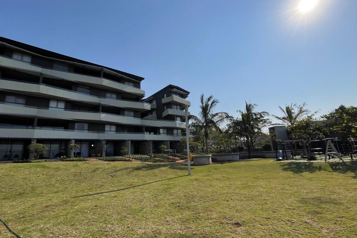 A view of the apartment building exterior featuring multi-level balconies with glass balustrades, stone cladding accents, and a well-maintained communal garden area.