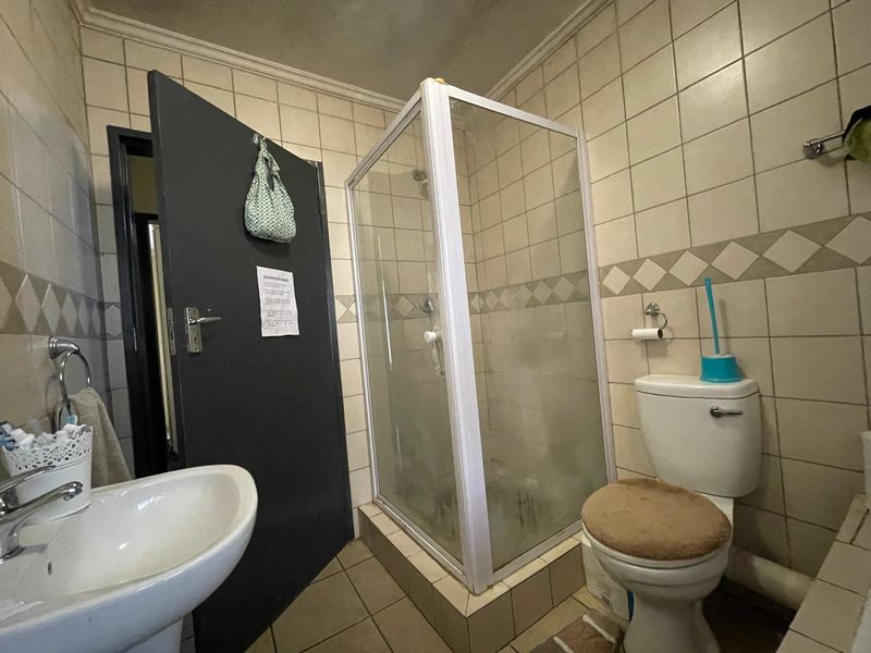 A functional bathroom featuring a corner shower enclosure, pedestal basin, and toilet with dated ceramic wall and floor tiling.