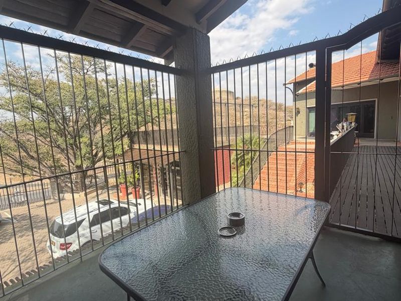 A covered balcony area featuring exposed timber beams and security bars, overlooking the property grounds.