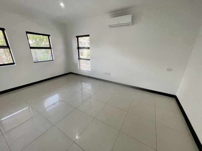A bright, empty bedroom featuring neutral tiled flooring, modern split-system air conditioning, and large windows with fitted blinds.