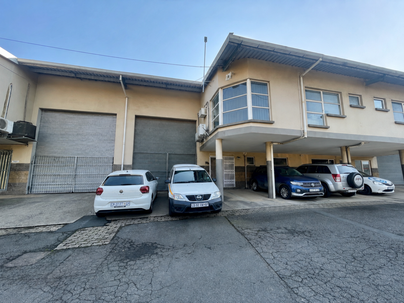 Front elevation of a mixed-use industrial building featuring roller shutter doors, covered parking area, and paved driveway access.