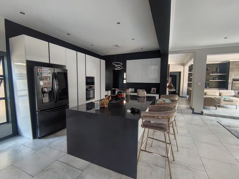 Modern open-plan kitchen featuring a large central island, high-gloss cabinetry, built-in appliances, and sleek tiled flooring, seamlessly connecting to the adjacent living area.