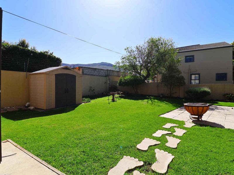 A private rear garden featuring a well-maintained lawn, paved patio area, and secure boundary walls with electric fencing.