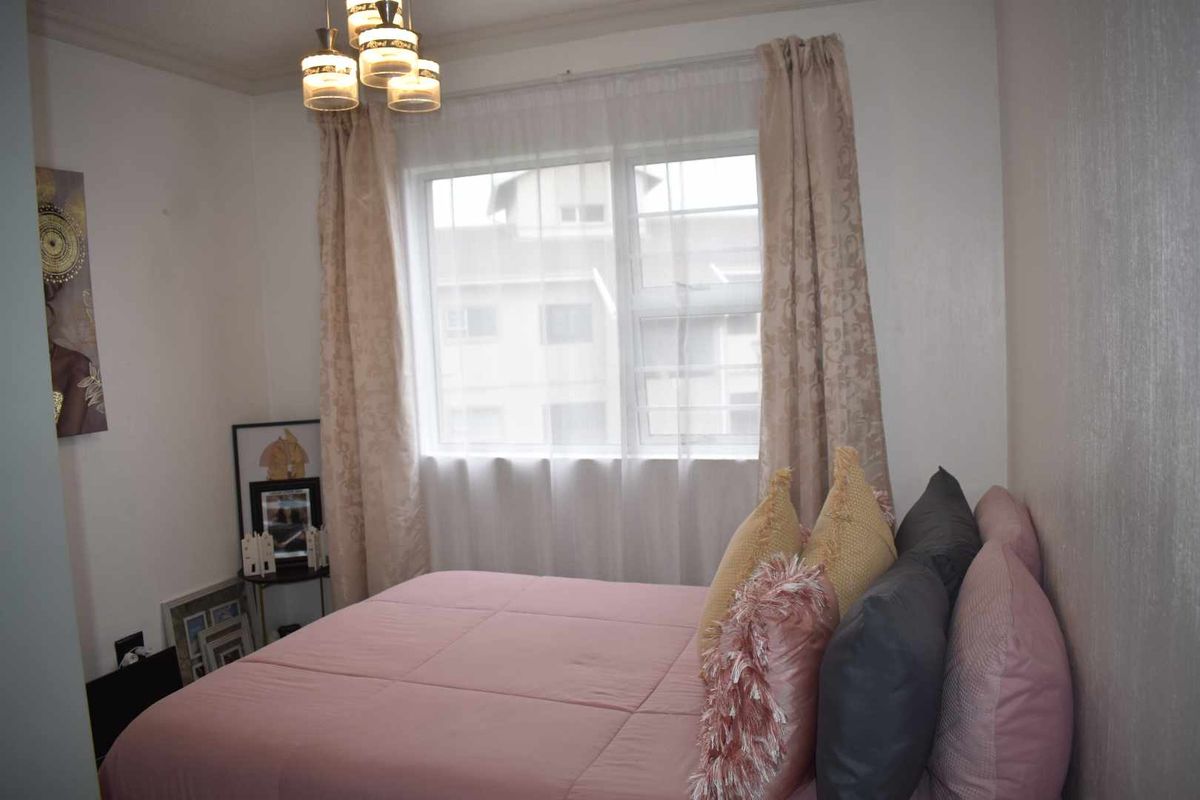A cozy bedroom featuring a large window with natural light, neutral wall finishes, and a central ceiling light fixture.