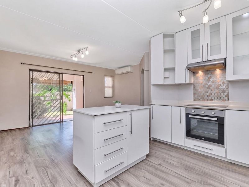 Modern open-plan kitchen and living area featuring white cabinetry, a central island, laminate flooring, and direct access to an outdoor patio area.