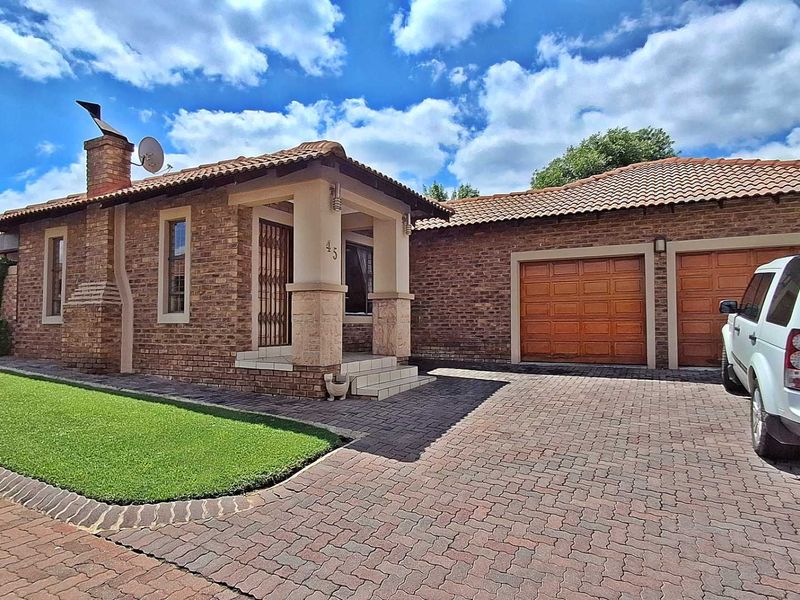 Front elevation of a brick townhouse featuring a double garage, paved driveway, and a covered entrance porch.