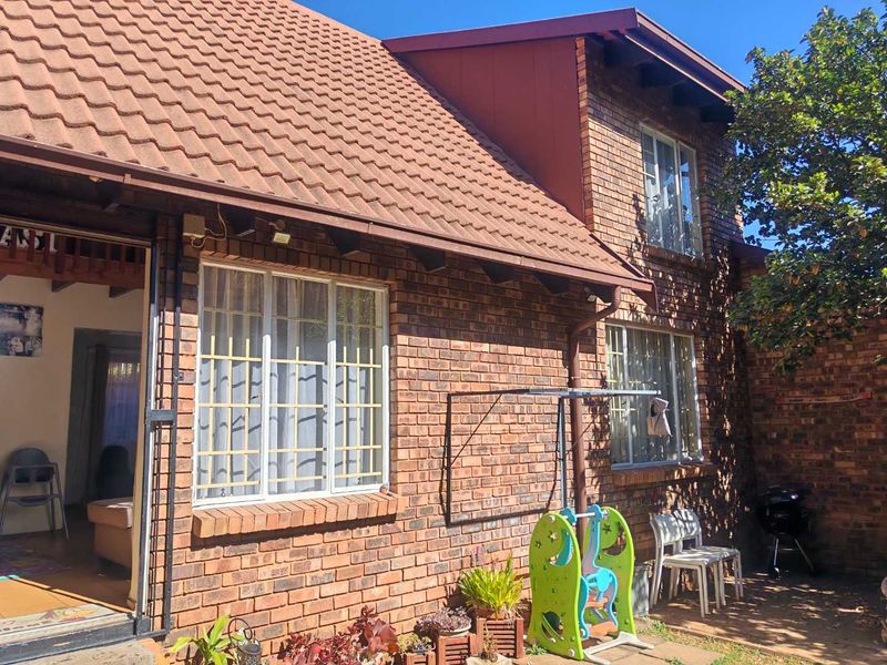 Rear view of a face brick townhouse featuring a tiled roof, security bars on windows, and a paved outdoor area.